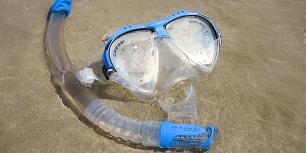 A blue and white mask with a tube of water on the beach.